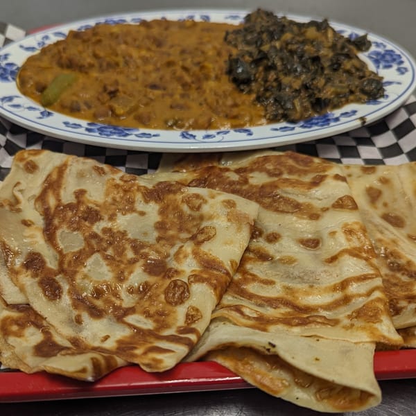African flatbread with a plate of stewed meat and greens in the background.