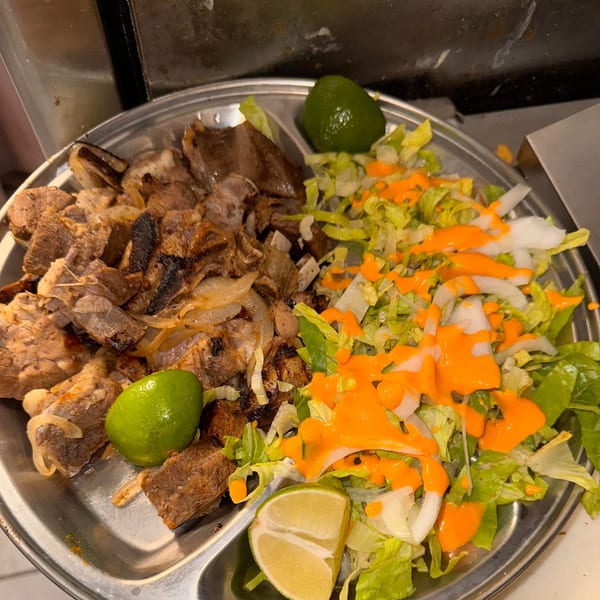 Halwo Kismayo Grill's grilled meat with onions, a side salad drizzled with orange sauce, and lime wedges.