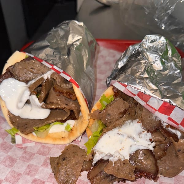 Two Halwo Kismayo Grill gyros, filled with meat, lettuce, and white sauce, on a red checkered tray.