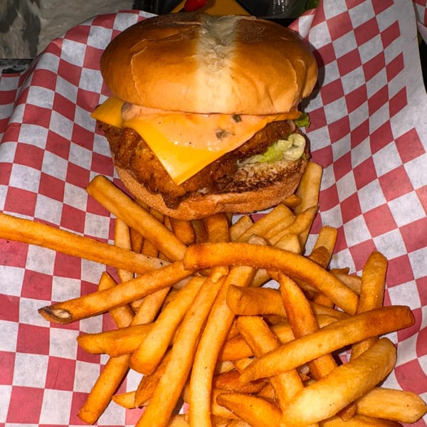 A fried chicken sandwich with cheese and lettuce, served with a side of golden fries.