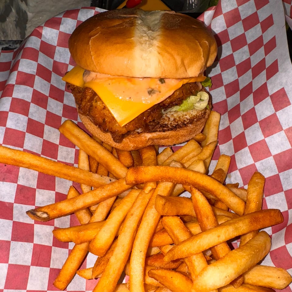 A fried chicken sandwich with cheese and lettuce, served with a side of golden fries.