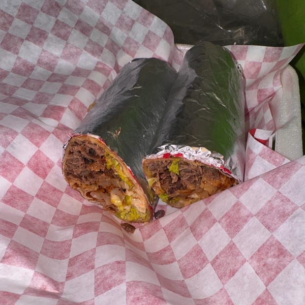 Two Halwo Kismayo Grill wraps, cut in half, revealing meat and vegetables, on checkered paper.