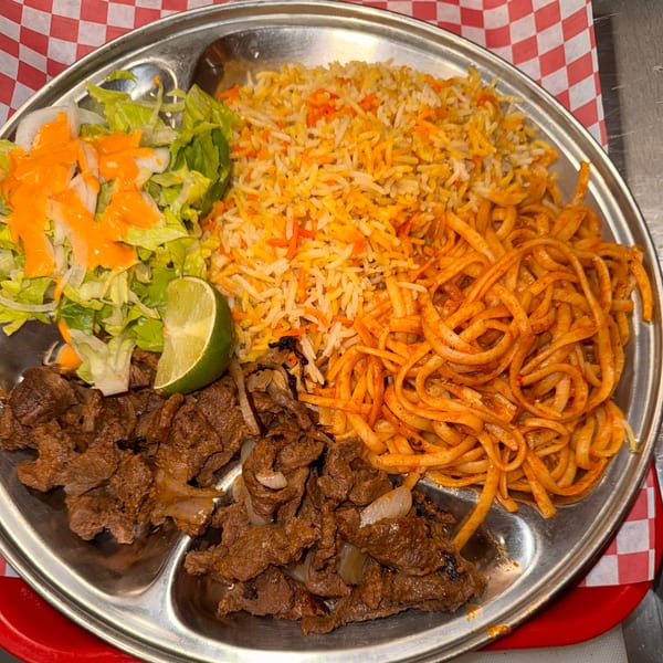 Halwo Kismayo Grill's African platter with rice, noodles, grilled meat, salad, and a lime wedge.